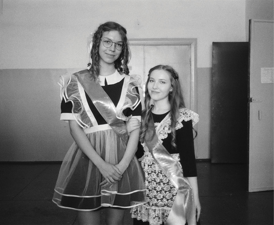 Two school girls in dresses, looking at camera.