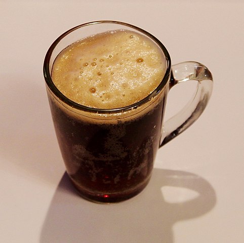 A clear mug of foamy brown liquid. 