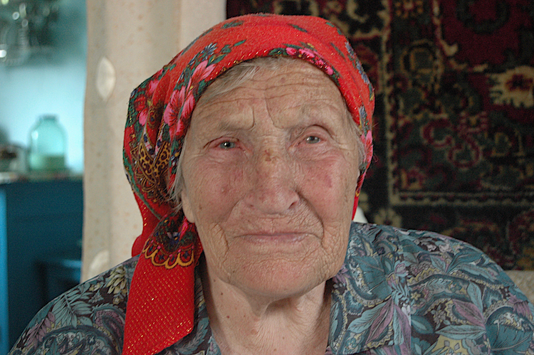 A Russian granny stares directly at the camera with a red scarf on her head.