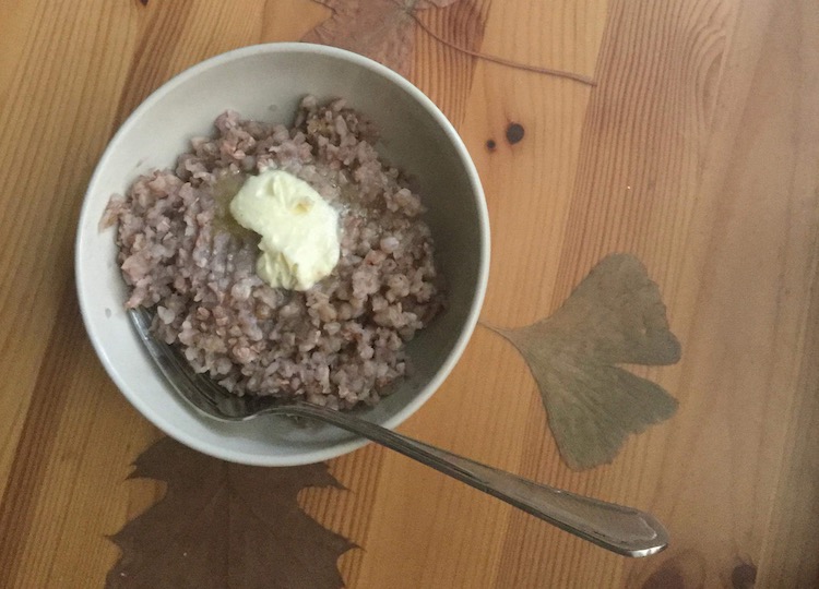 A bowl of buckwheat kasha sits on a table with a big glob of butter on top.
