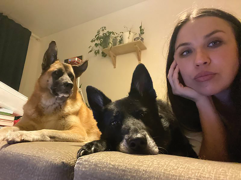 Woman on bed with two dogs, looking at camera.