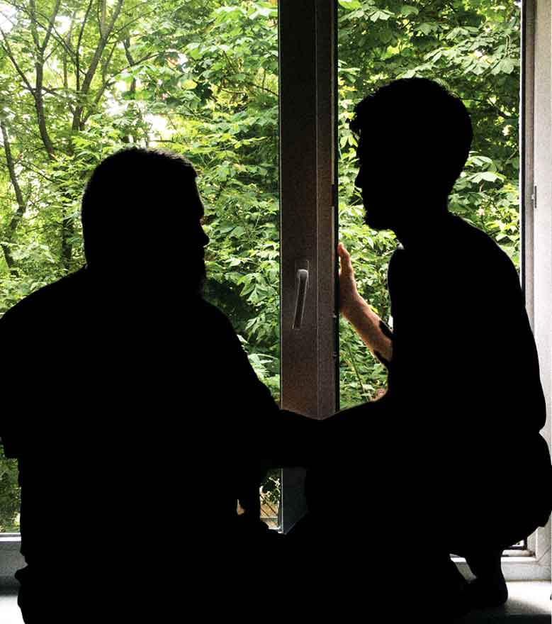 Two men sitting before a window.