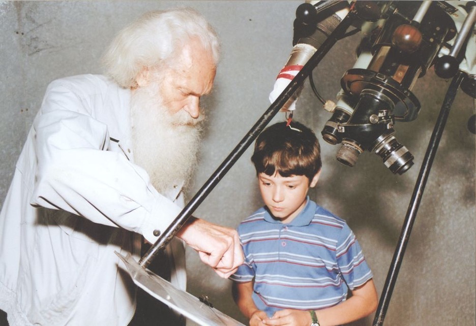 Older astronomer showing a child a telescope.