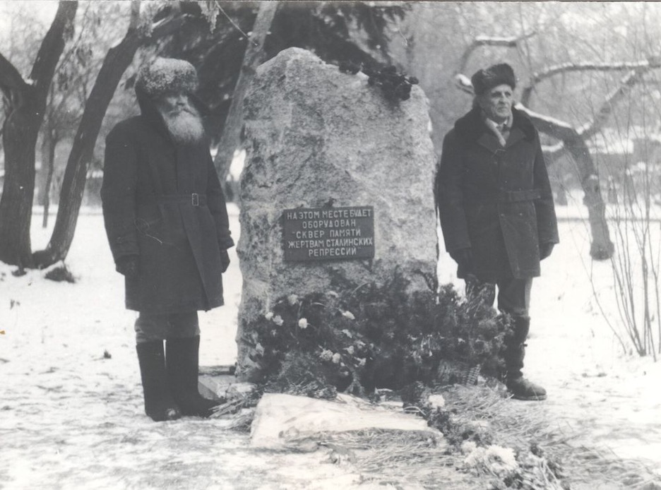 Two men standing alongside a gulag monument.